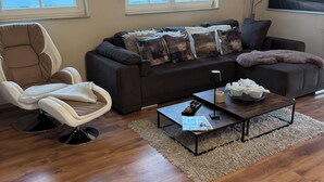 A living room with a sofa, armchair, coffee table, and a TV on the wall. - Modern, spacious, high quality furnished, apartment for 2-3 people (Sehlen)