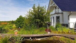 A house with a blue-tiled roof, a small pond, and lush greenery. - Modern, spacious, high quality furnished, apartment for 2-3 people (Sehlen)
