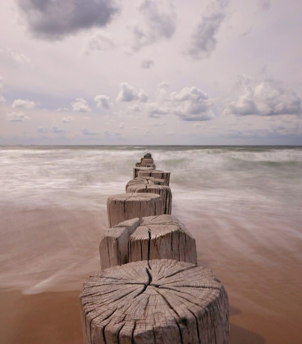 A wooden jetty extending into the ocean with a cloudy sky above.
