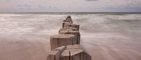 A wooden jetty extending into the ocean with a cloudy sky above.