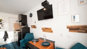 Un espace de vie moderne et compact comprenant un coin repas, une kitchenette et un téléviseur à écran plat fixé au mur.