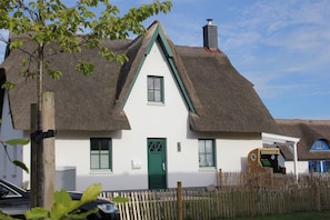 A traditional thatched-roof house with a green door, white walls, and a wooden fence in front.