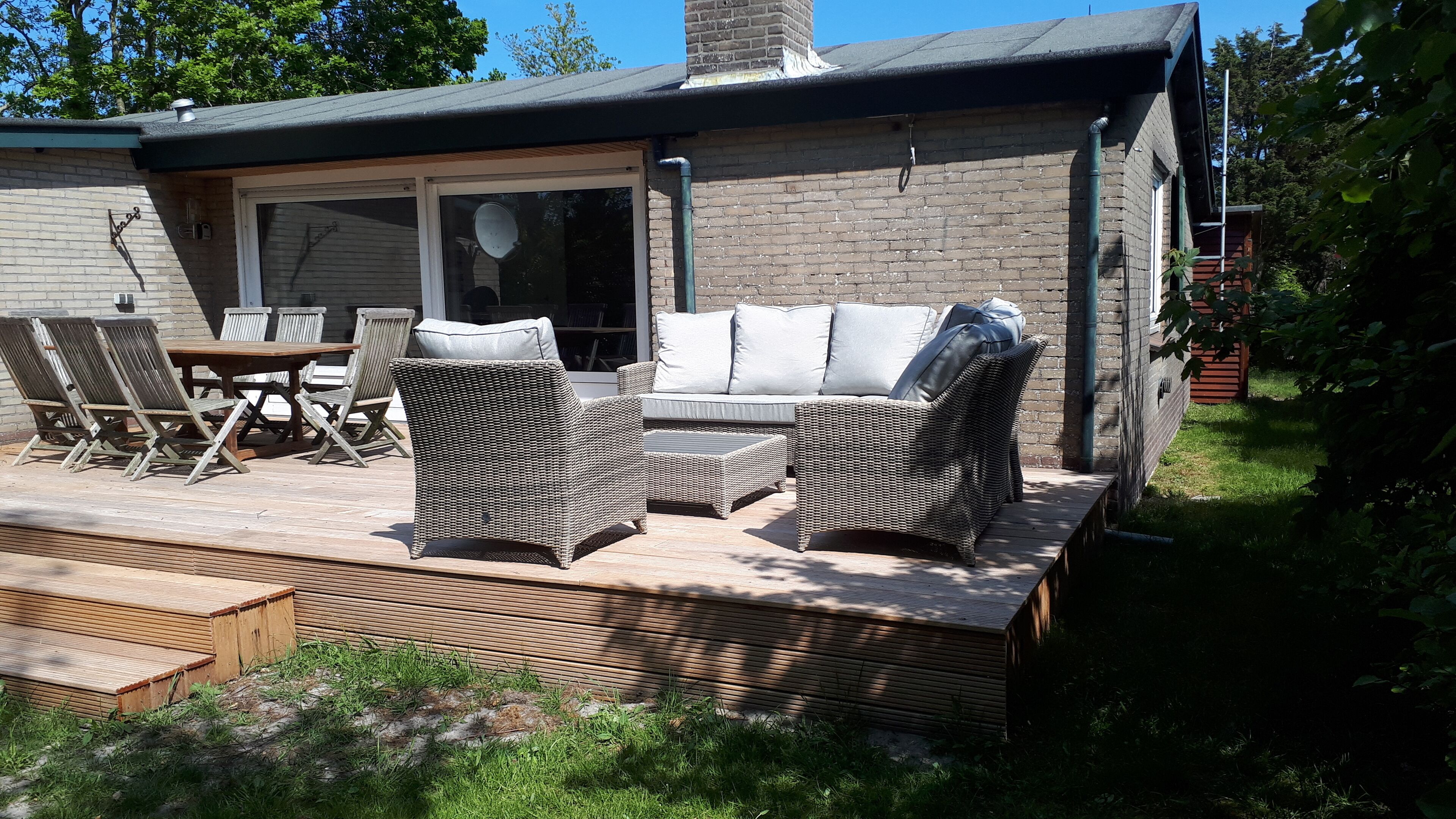 An outdoor patio with wicker furniture, a wooden table, and a glass door leading to the interior.