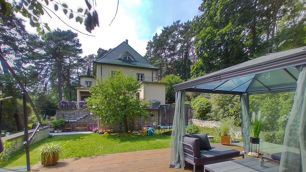 A wooden deck with outdoor furniture, a covered seating area, and a view of a house in the background.
