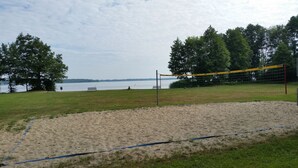 A beach volleyball court with a net, sand, and a grassy area.