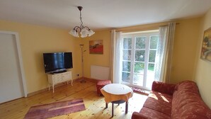 A living room with a television, a white table, a red sofa, and a large window.