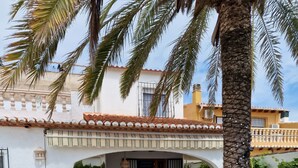 A courtyard with a tiled floor, a palm tree, and a covered seating area with chairs. - HOLIDAY HOUSE DIRECTLY BY THE SEA (Oliva Playa)