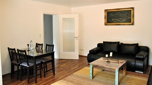 Una sala de estar con una mesa de comedor, sofá de cuero negro y un cuadro en la pared.