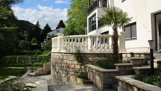 Un edificio moderno con una escalera de piedra, un balcón y un jardín con una palmera.