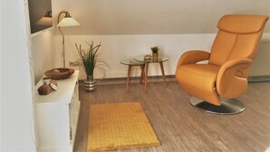 A modern living room with a leather armchair, a small glass table, a floor lamp, and a potted plant.