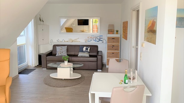 A modern living room with a brown leather sofa, a glass coffee table, and a white dining table with chairs. There is a ceiling light fixture above the sofa.