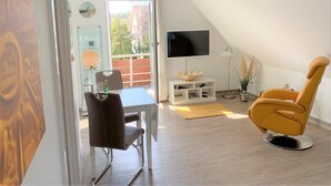 A modern living room with a dining area, a flat-screen TV, and a yellow armchair.