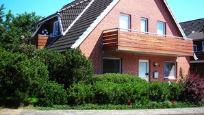 A red brick house with a sloped roof, a wooden balcony, and a small window.