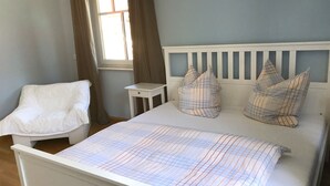 A bedroom with a white bed, a white chair, and a small bedside table. - Living in a fantastic location in the historic center of Thurnau (Thurnau)