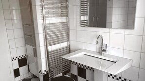 A modern bathroom with a white sink, chrome fixtures, and a checkered floor pattern. - Living in a fantastic location in the historic center of Thurnau (Thurnau)