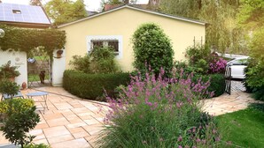 A yellow house with a solar panel, a garden with purple flowers, and a paved patio area. - Living in a fantastic location in the historic center of Thurnau (Thurnau)