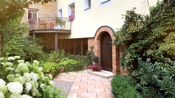 A courtyard with a brick entrance, a balcony with red chairs, and various plants and flowers. - Living in a fantastic location in the historic center of Thurnau (Thurnau)