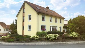 A two-story house with a sloped roof, multiple windows, and a garden with various plants and flowers. - Living in a fantastic location in the historic center of Thurnau (Thurnau)