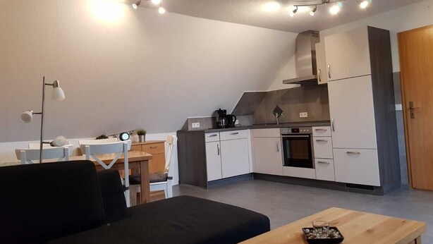 Una cucina moderna con mobili bianchi, forno integrato e macchina per il caffè. In primo piano, un tavolo di legno con un vassoio di snack.