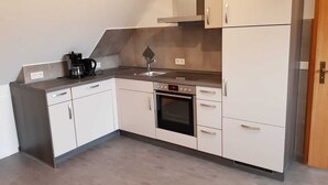Una cucina compatta con mobili bianchi, forno integrato, macchina da caffè e lavello.