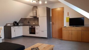 Una cucina compatta con elettrodomestici moderni, un'area pranzo con tavolo in legno e una TV su un mobile in legno.