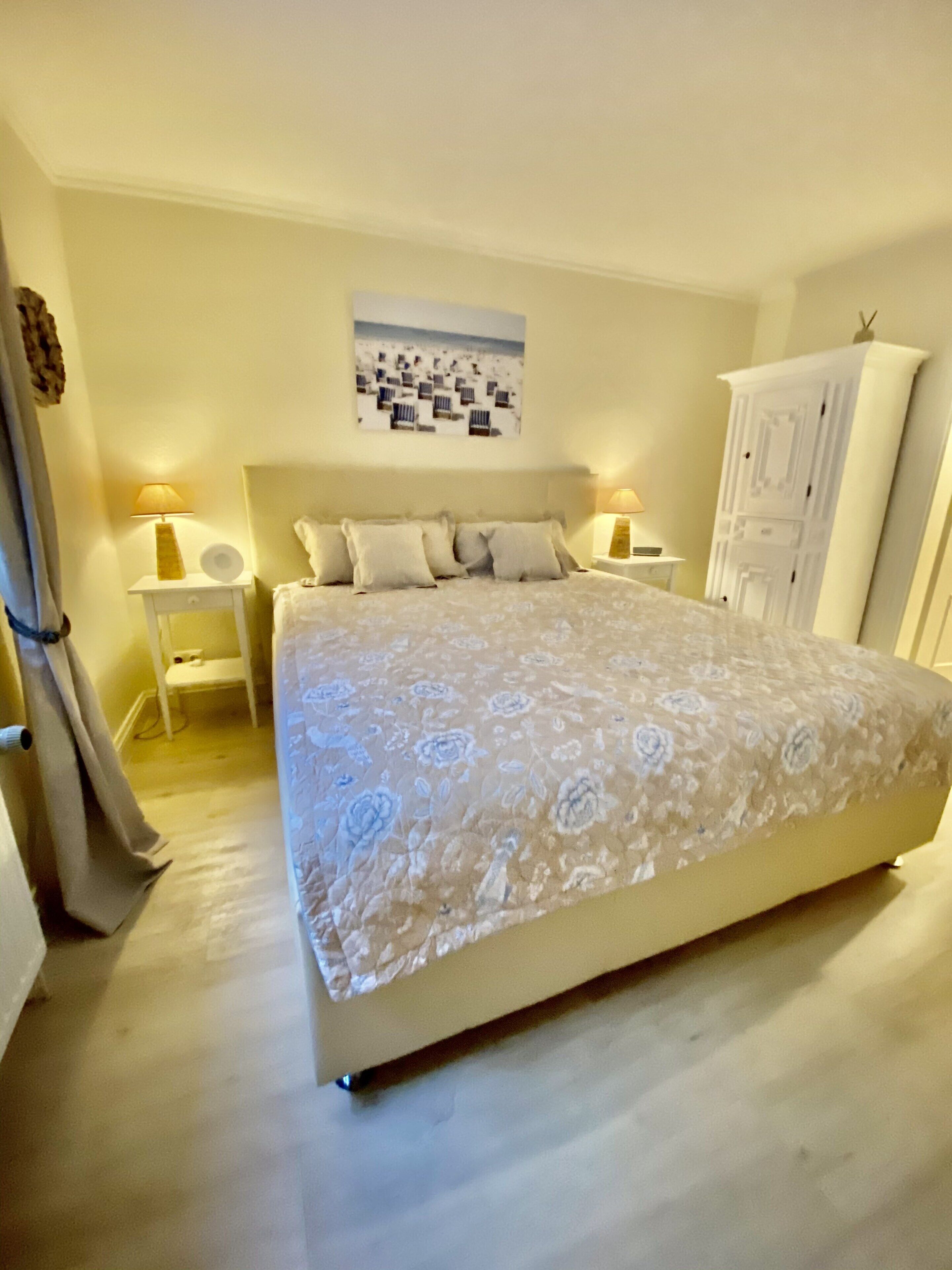 A bedroom with a bed, bedside lamps, a nightstand, a wardrobe, and a wall-mounted picture.