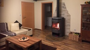 A cozy living room with a fireplace, a sofa, a coffee table, and a cabinet with glassware. - Newly renovated apartment f. d. high standards in an idyllic secluded location (Zachenberg)