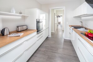 Une cuisine moderne avec des meubles blancs, un plan de travail en bois, un grille-pain, une bouilloire et un évier rempli de légumes.
