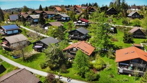 Ein Wohngebiet mit Häusern mit geneigten Dächern, einige mit Solaranlagen, umgeben von Grünflächen und einem klaren Himmel.