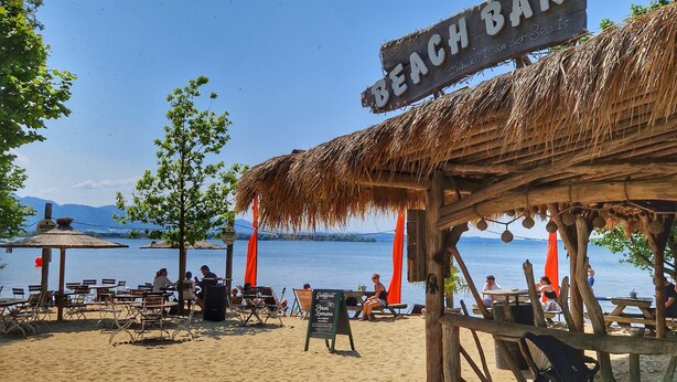 Eine Strandbar mit Reetdach, Sitzgelegenheiten im Freien und Blick auf das Meer.