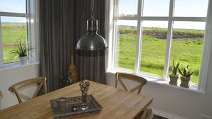 Ein Essbereich mit Tisch, Stühlen, einer Hängelampe und Blick auf ein grünes Feld durch große Fenster.