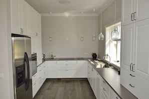Cozinha moderna com armários brancos, eletrodomésticos de aço inoxidável e iluminação pendente.