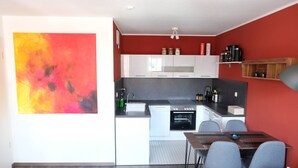 Une cuisine moderne avec des meubles blancs, un four encastré et un coin repas avec des chaises grises.