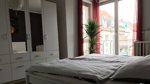 Une chambre à coucher avec un lit, une armoire, une fenêtre avec des rideaux et une plante en pot.