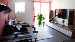 Un salon moderne comprenant un canapé, une table à manger, un téléviseur et une grande fenêtre avec des rideaux.