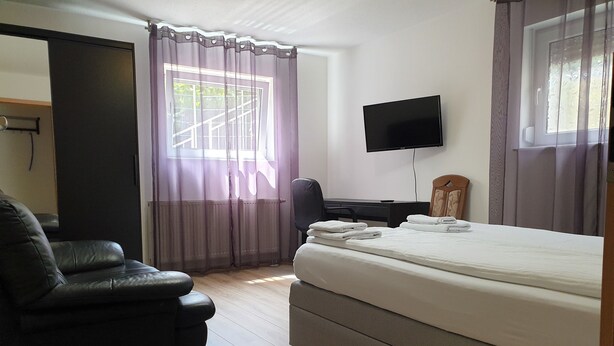 Ein Hotelzimmer mit Bett, Schreibtisch, Stuhl, Fernseher und einem Fenster mit Vorhängen.
