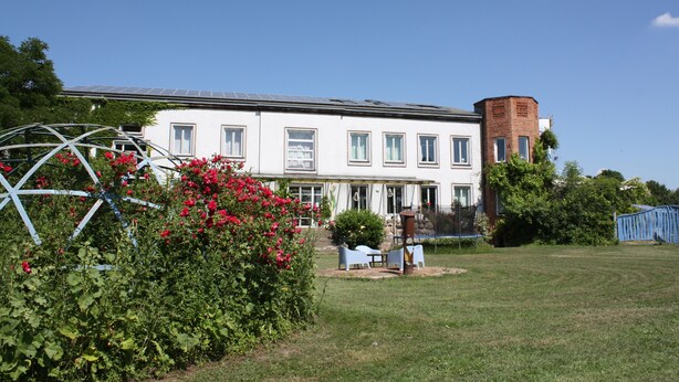 A white building with a brick tower, a garden with red flowers, and a blue fence. - Room in an old manor with an artistic atmosphere (neukalen)