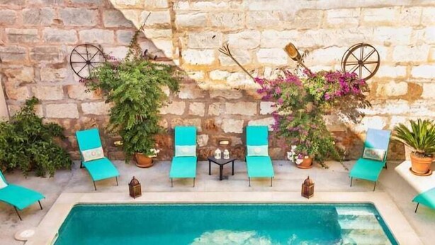 A poolside area with a stone wall, lounge chairs, and potted plants. - Can Caragol (Sineu)