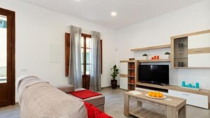 A modern living room with a sofa, a coffee table with fruit, a TV, and a bookshelf. - Can Caragol (Sineu)