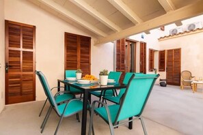 A dining area with a table set for four, surrounded by teal chairs, wooden shutters, and a ceiling with exposed beams. - Can Caragol (Sineu)