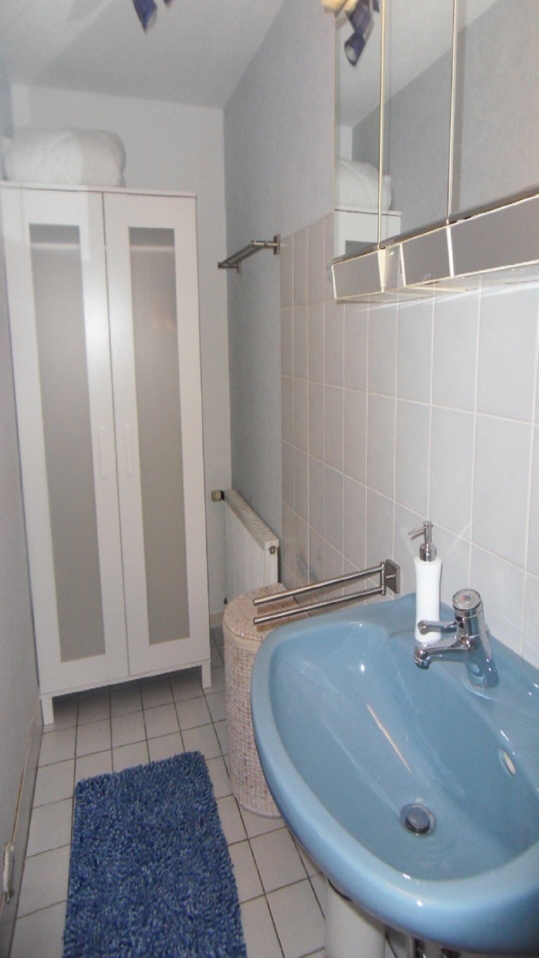 Ein Badezimmer mit blauem Waschbecken, weißen Fliesen, einem Handtuchhalter und einem Schrank.