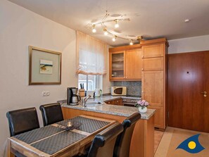Cocina compacta con armarios de madera, microondas, cafetera y comedor con mesa y sillas.