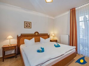 Un cuarto de hotel con una cama grande, dos mesitas de noche, una lámpara de noche, un cuadro enmarcado en la pared y una ventana con cortinas.