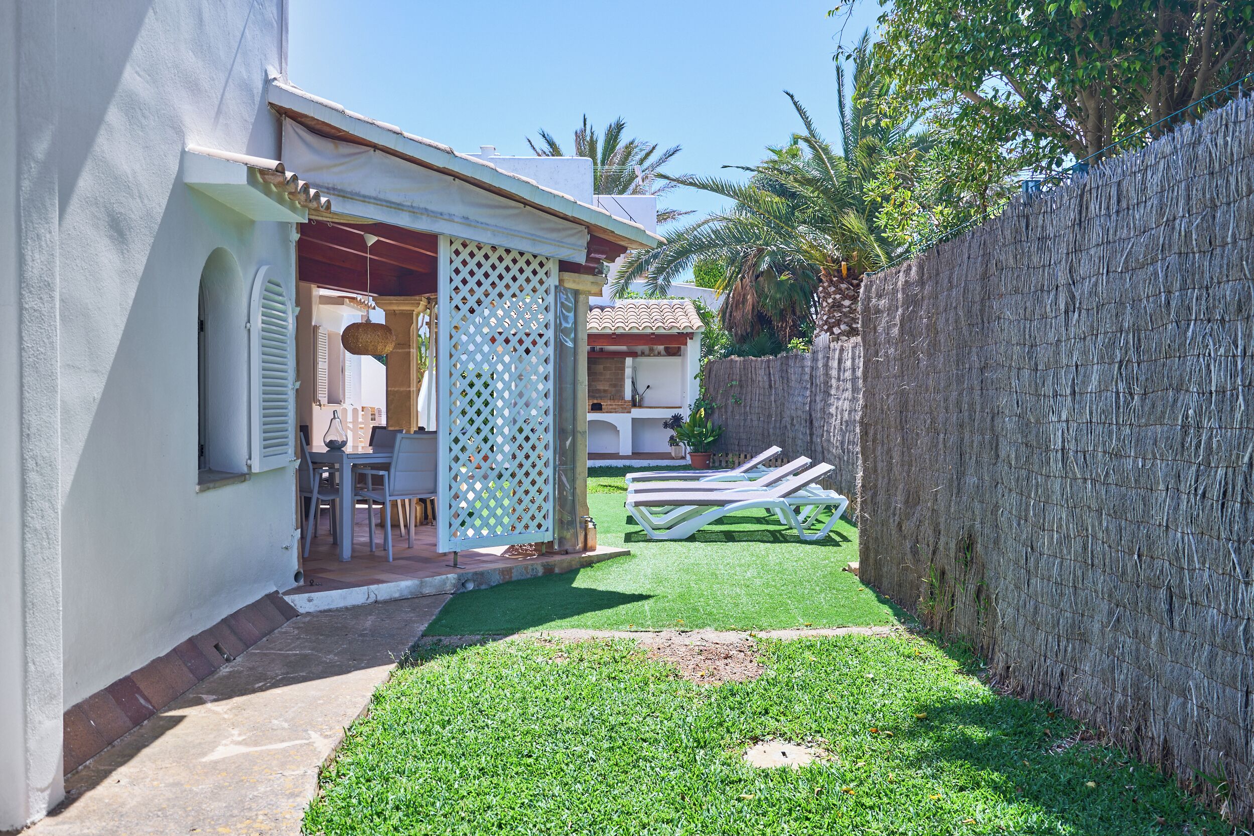 Un jardin à l’arrière de la maison, avec une terrasse, une clôture blanche et un petit potager.