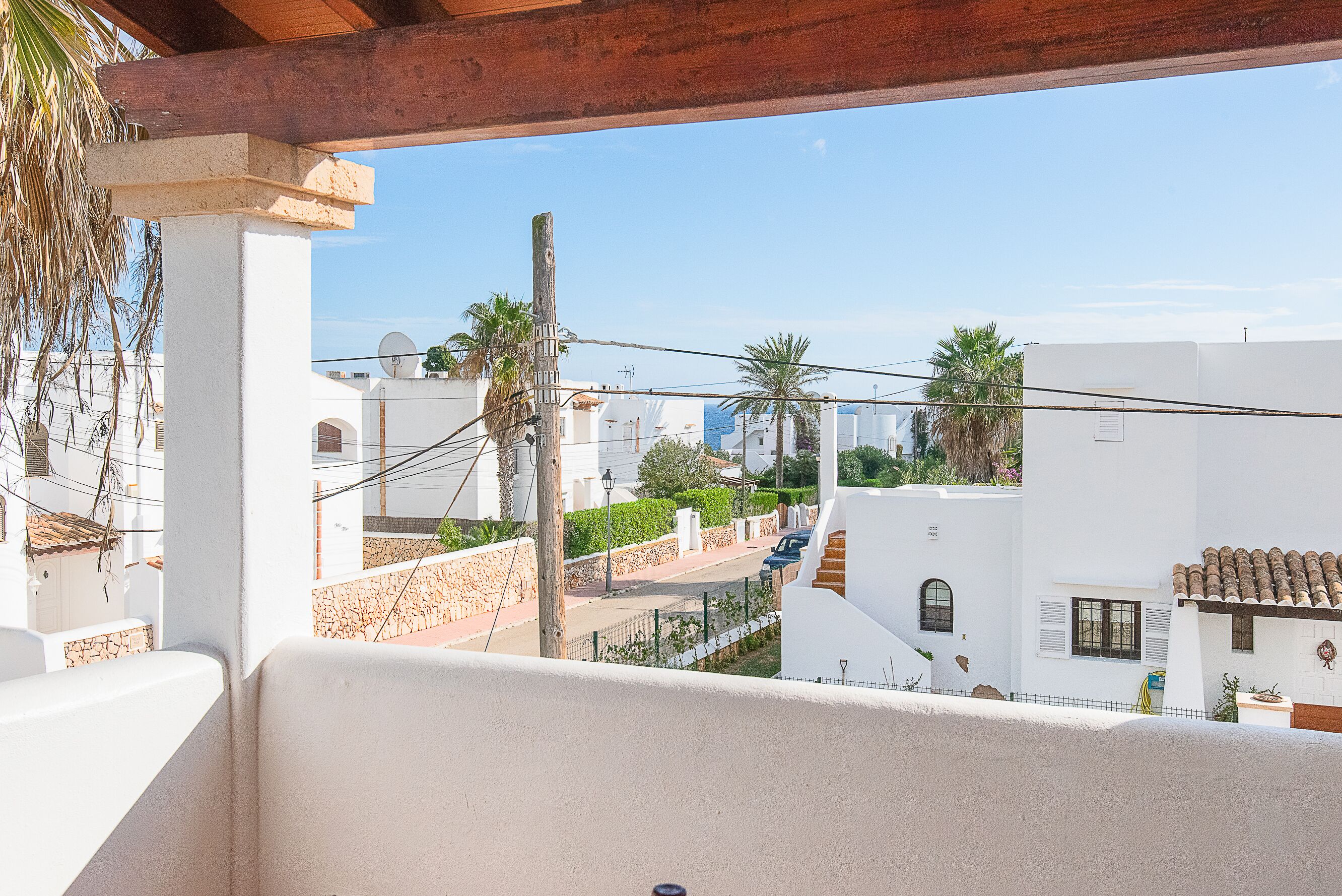 Un balcon donnant sur un quartier résidentiel, avec des bâtiments blancs, des palmiers et un ciel dégagé.