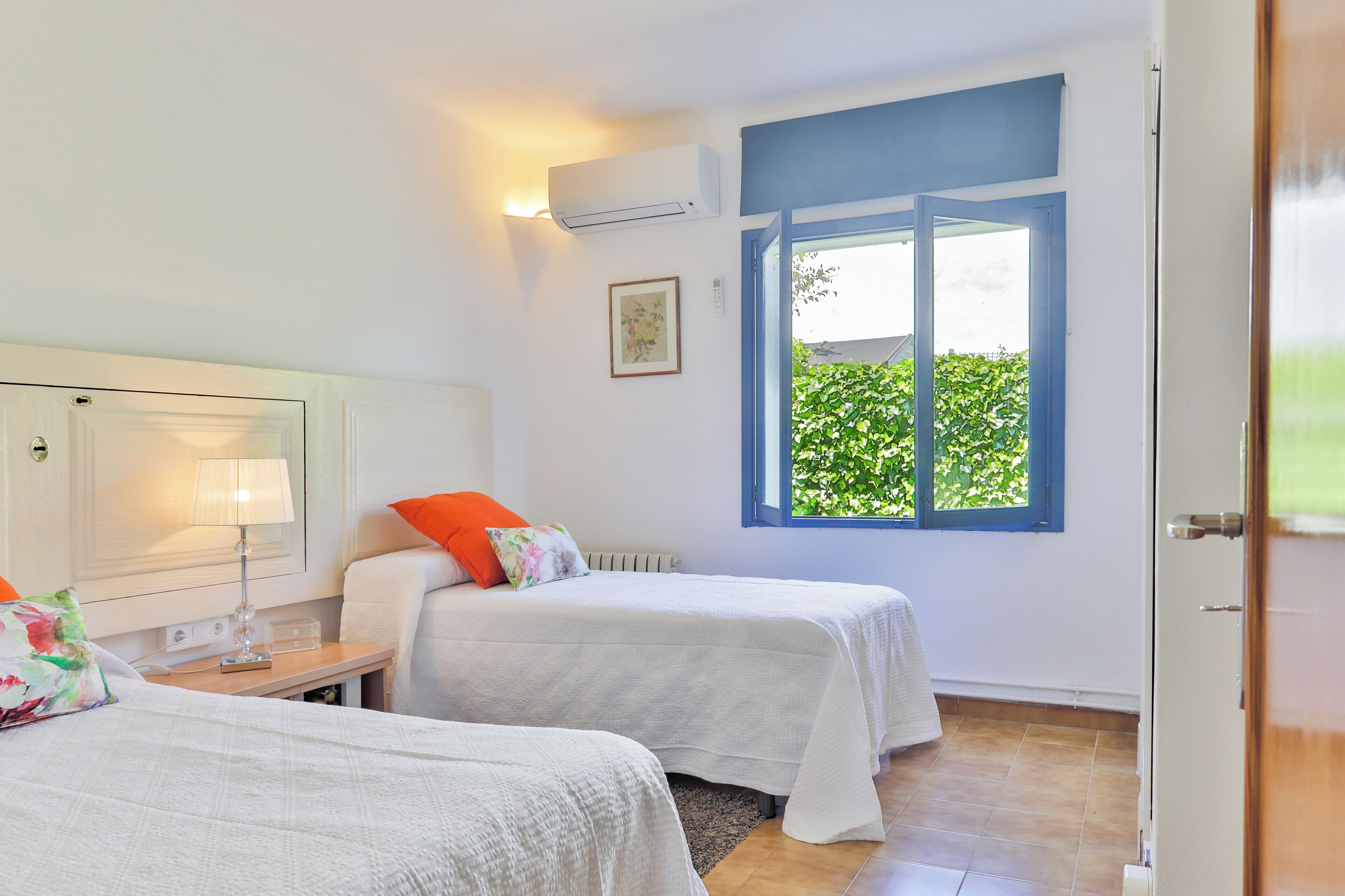Ein Zimmer mit zwei Betten, einem Fenster mit blauen Rollläden, einem Heizkörper und einer Wand-Klimaanlage.