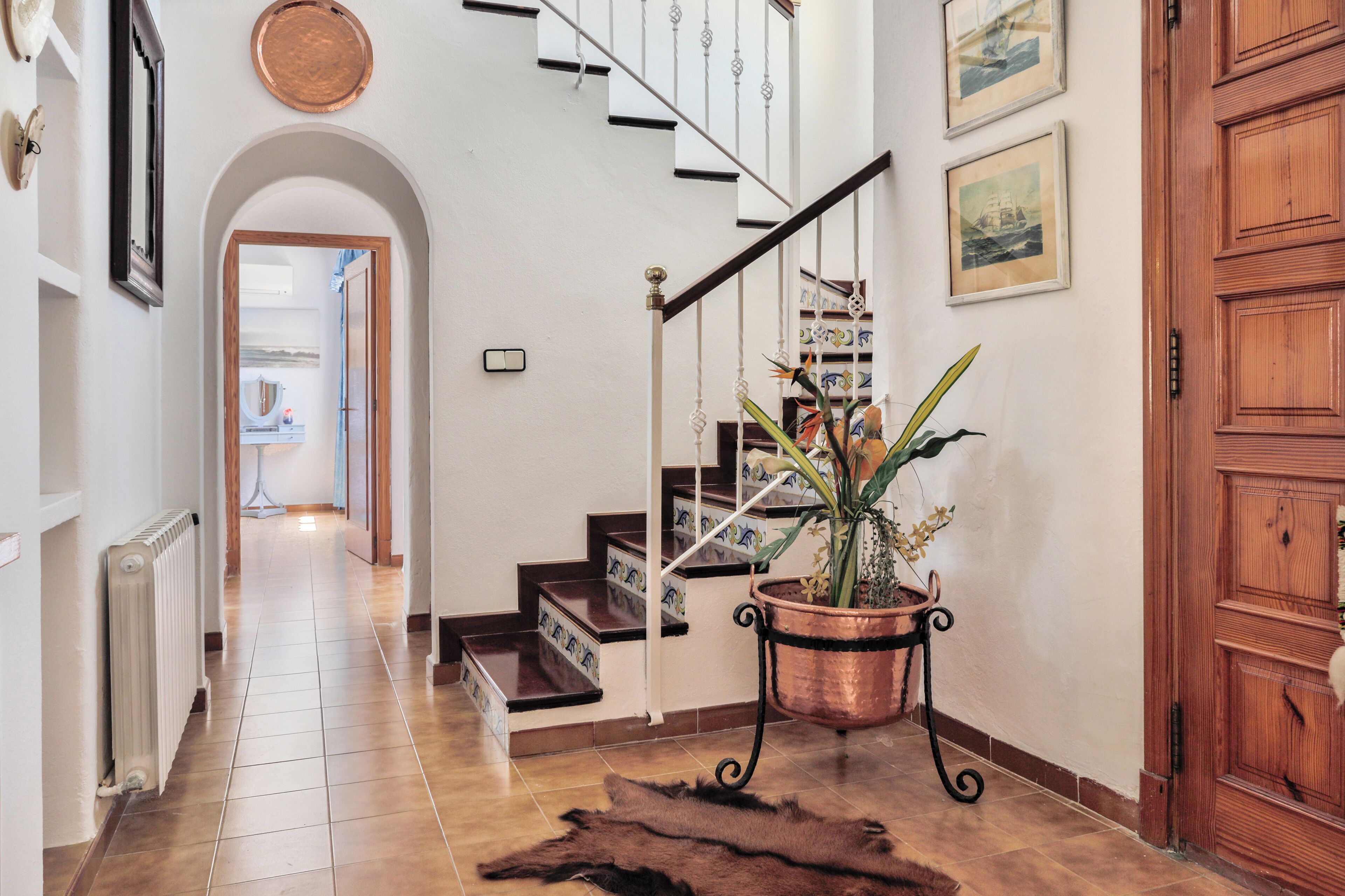 A hallway with a staircase, a radiator, a potted plant, and a wooden door.