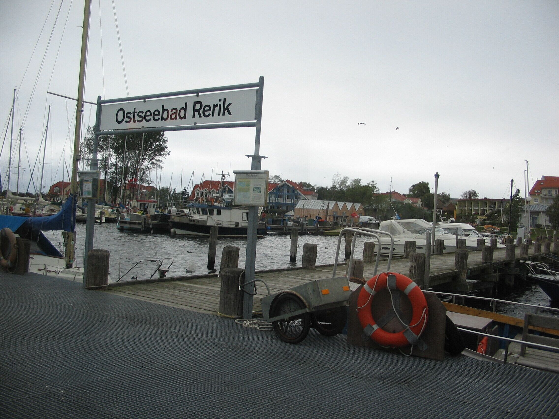 A marina with boats docked, a sign reading "Ostseebad Rerik", and a lifebuoy on the dock.
