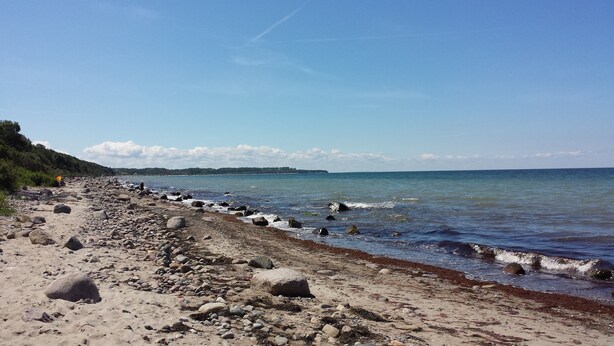 A rocky beach with waves crashing onto the shore, a clear sky, and a distant landmass.