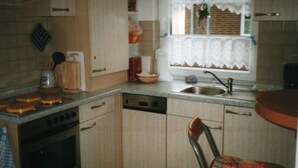 A compact kitchen with a dishwasher, stove, and a window with lace curtains.
